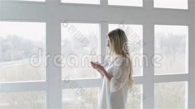 一个穿着白色时尚连衣裙的女孩正在手机上输入号码，并在窗户附近交谈。